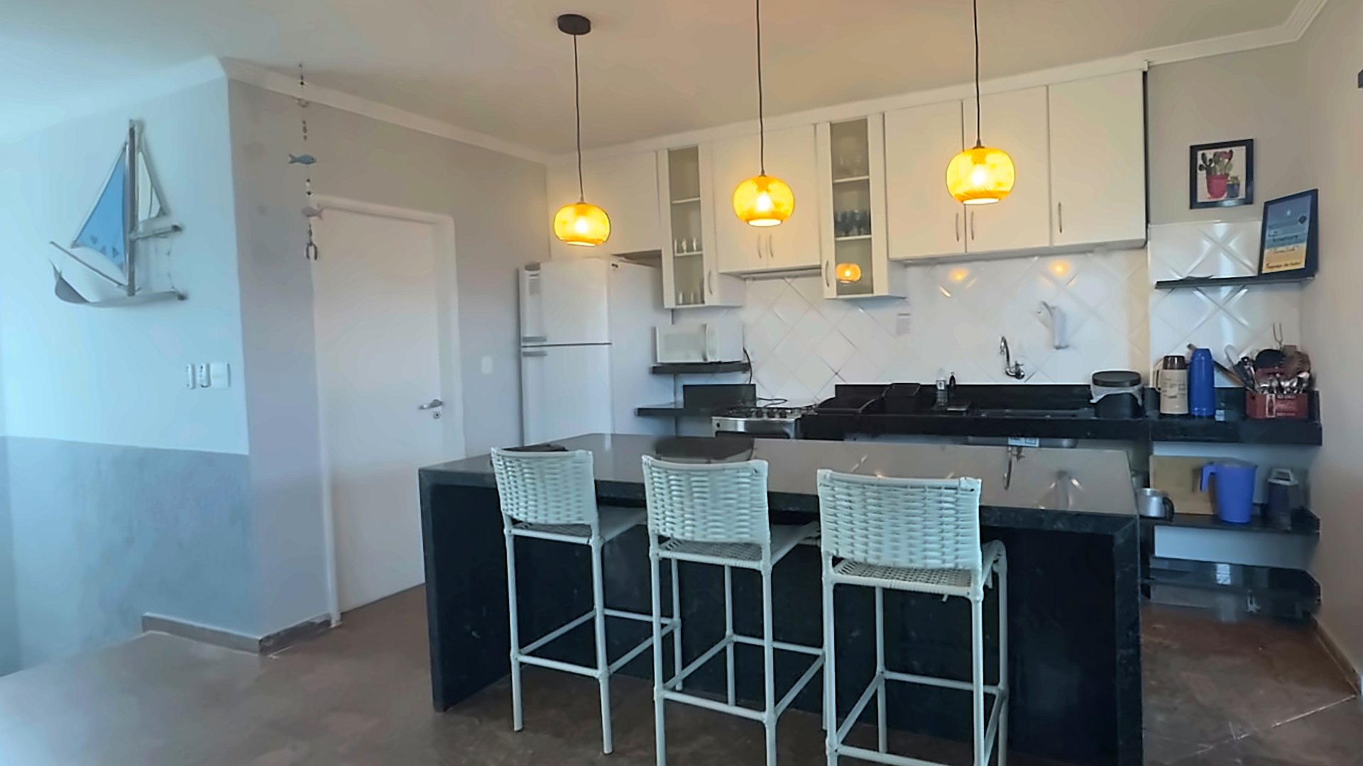Cozinha do piso superior com ilha de granito preto, banquetas e pendentes